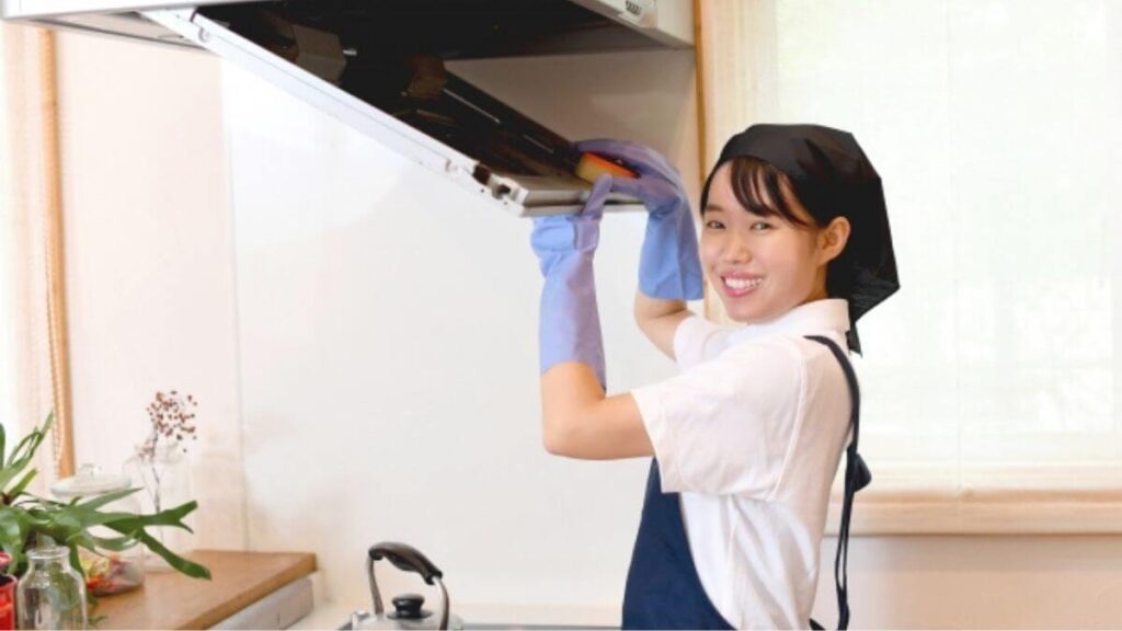笑顔で換気扇掃除をするクリーニング業者の女性