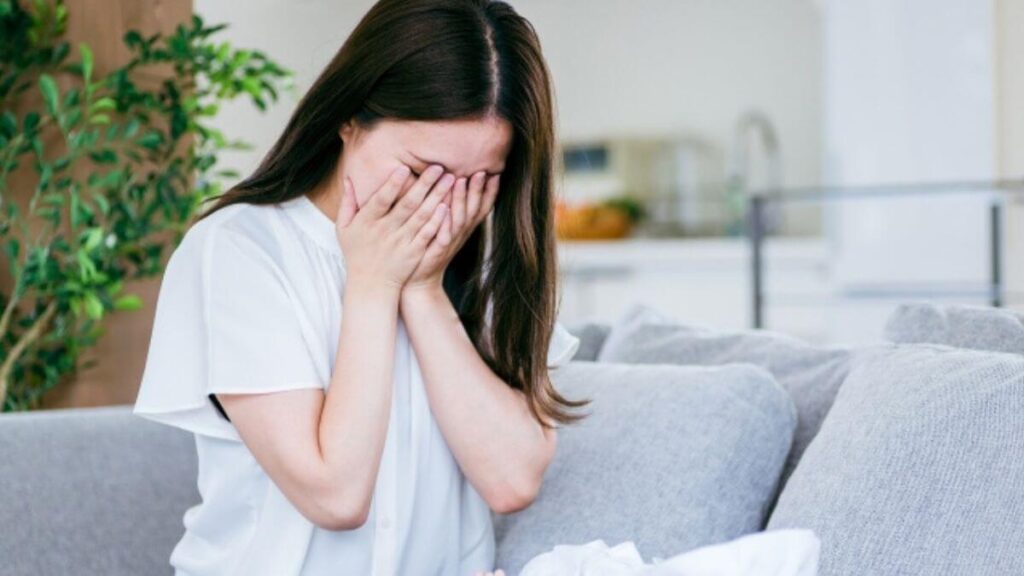 ソファーで手を押さえて落ち込む若い女性