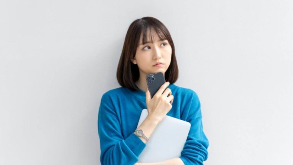 室内でスマホを頬に置き考える女性