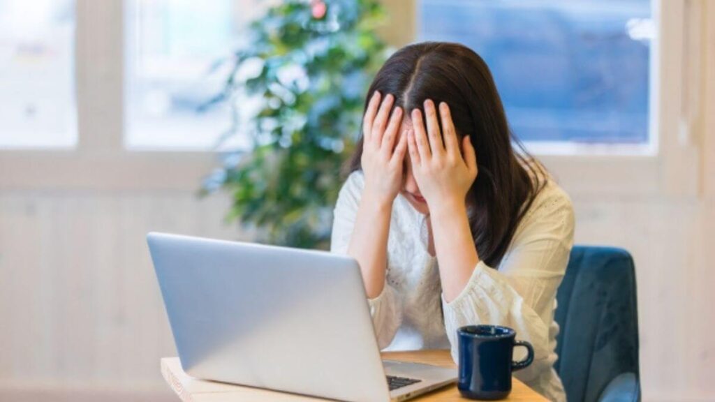 自宅のパソコン前で頭を抱える若い女性