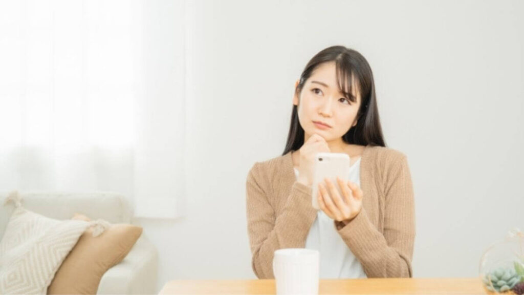 室内でスマホを持ち考えている若い女性