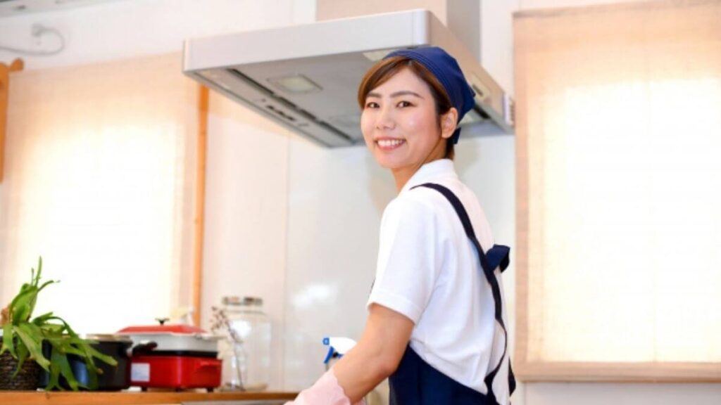笑顔で換気扇掃除をするハウスクリーニング業者の女性