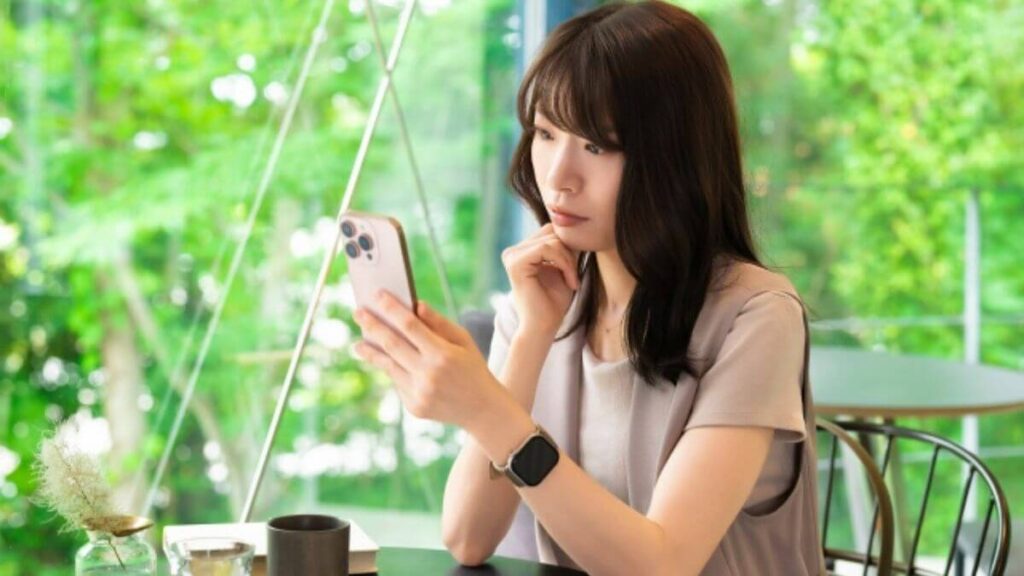 部屋でスマホを見ながら悩む若い女性