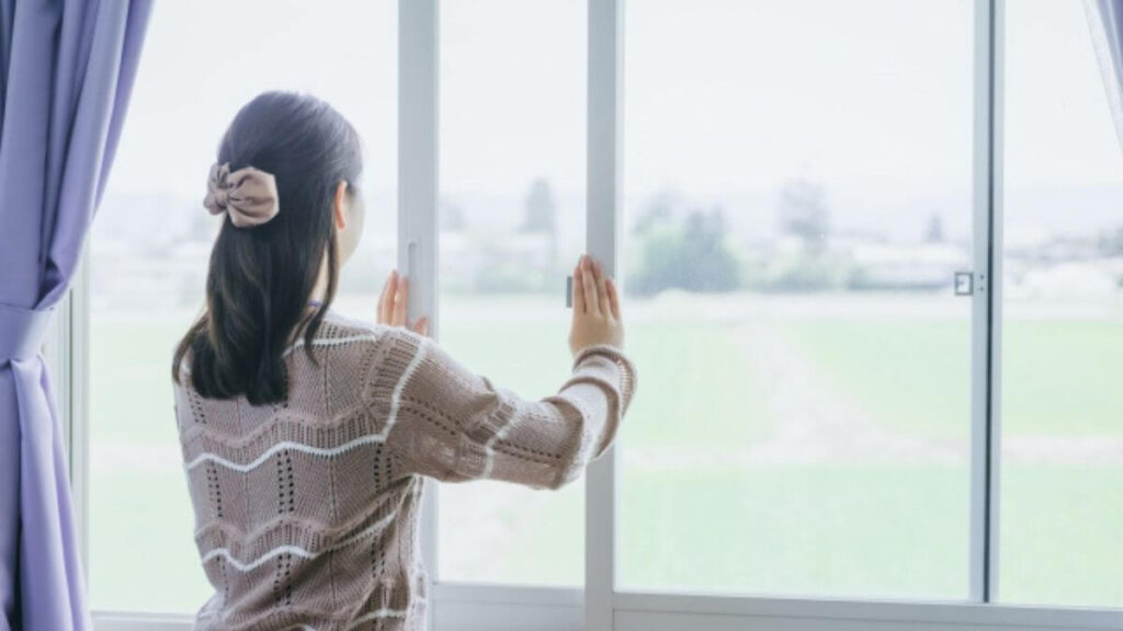部屋の窓を開ける若い女性