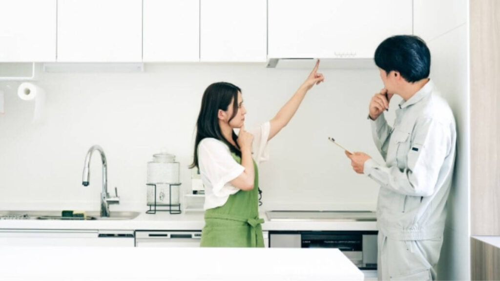 自宅の換気扇を業者の男性に見せる若い女性