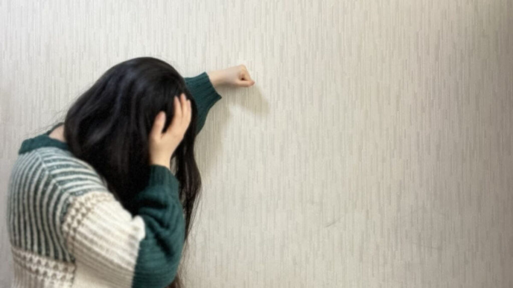 壁にもたれかかり体調が悪そうな女性