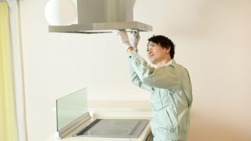 キッチンの換気扇を見る作業着姿の男性
