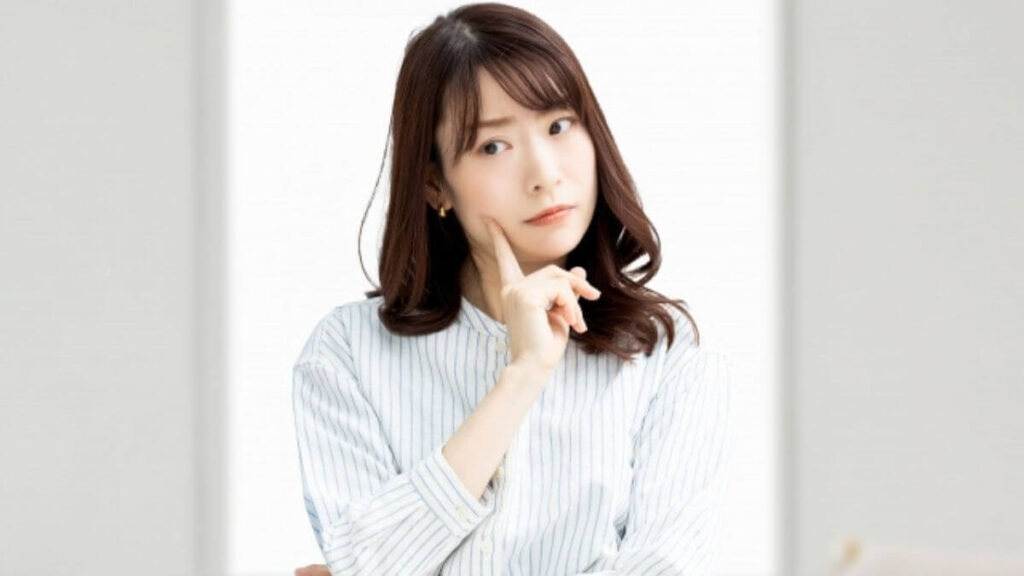 指を頬につけ考え事をする若い女性
