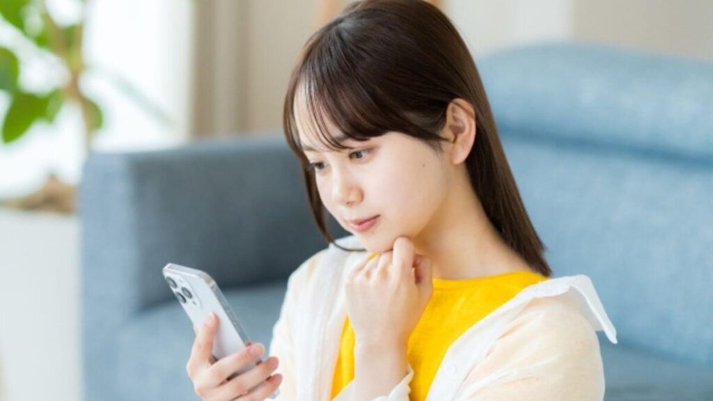スマートフォンを見ながら考え事をする若い女性