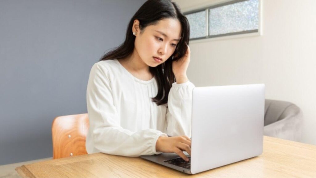 自室で頭を抱えながら仕事をする若い女性