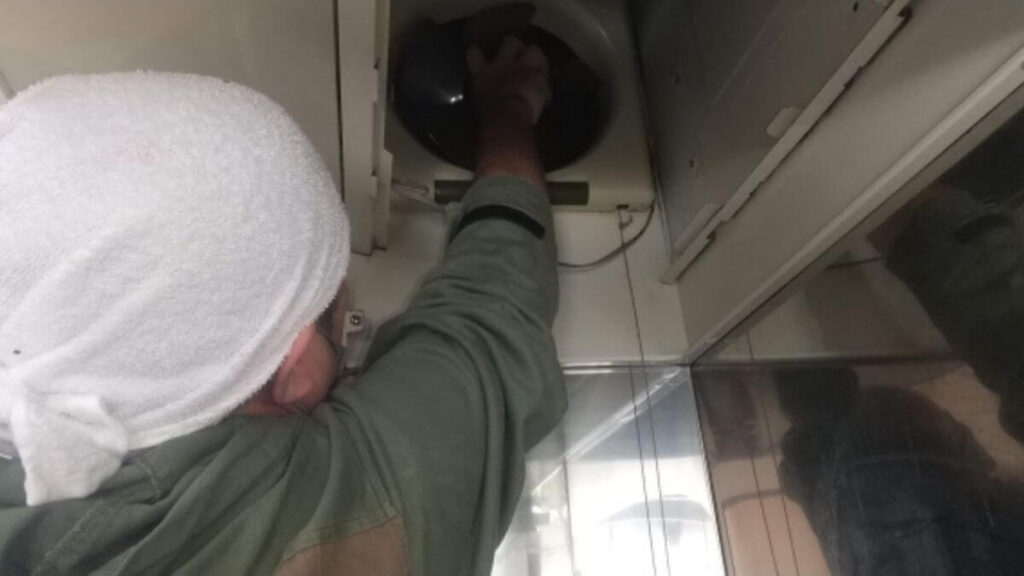 キッチンの換気扇を掃除する作業着姿の男性