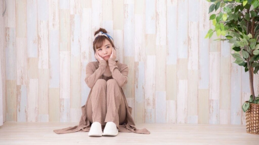 部屋の隅に座り不安そうに考える若い女性