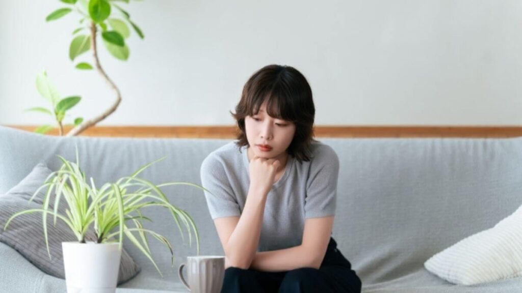 室内で座りながらくらい表情をする若い女性