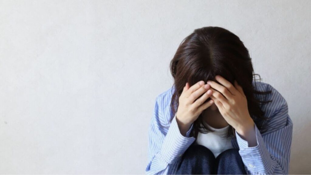 室内で頭を抱えて悩む若い女性